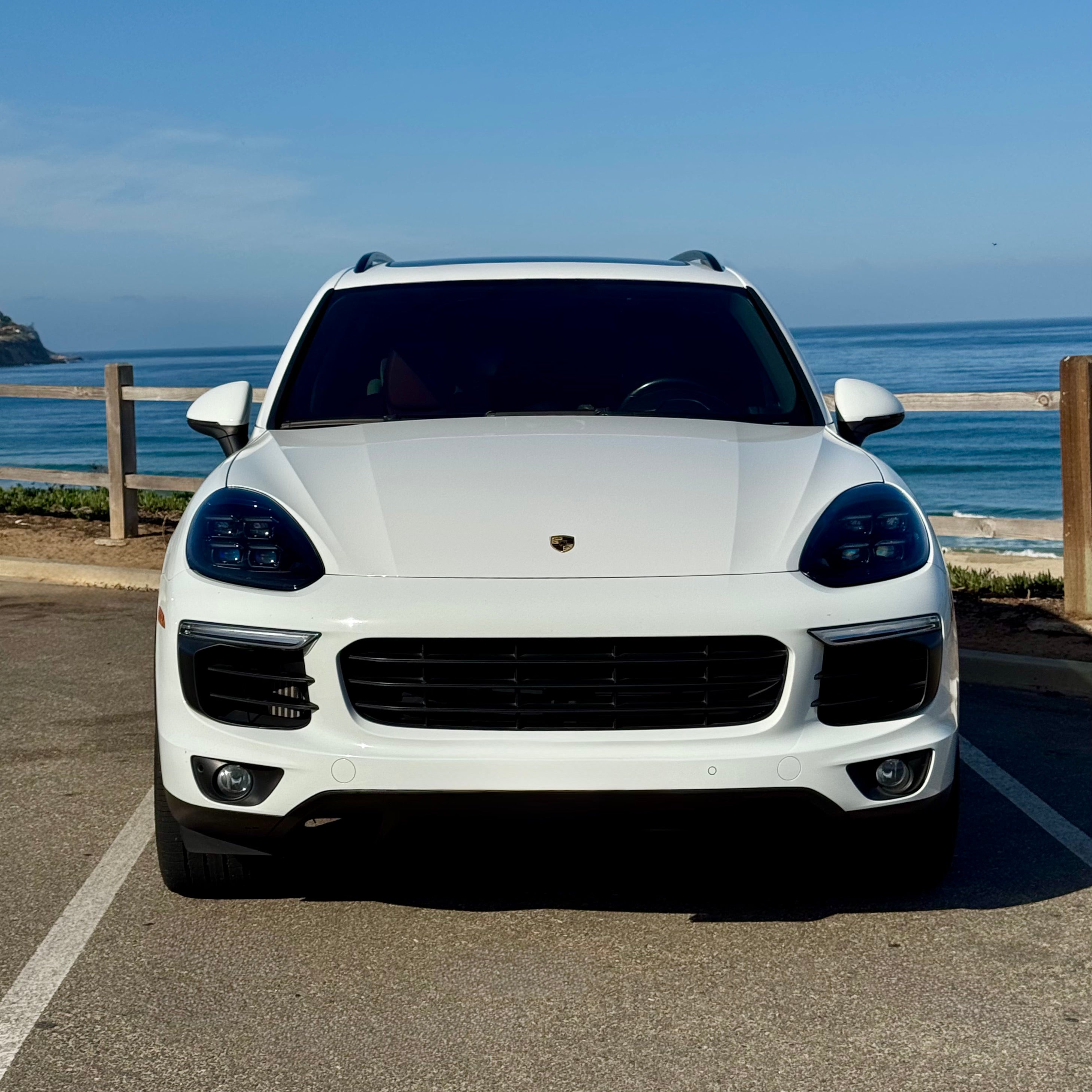 White Porsche Cayenne parked by a coastal road with ocean view
